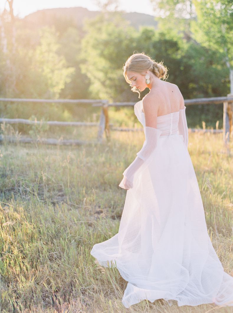 bride in grass field with hair in curled bun and earrings