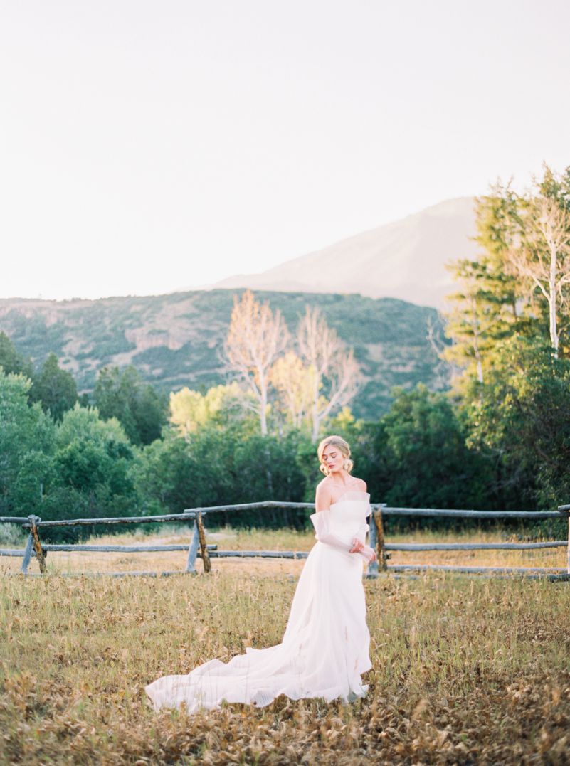 bride in white wedding gown in grassy field with mountains