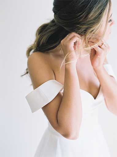 breautiful bride in white dress putting in an earring