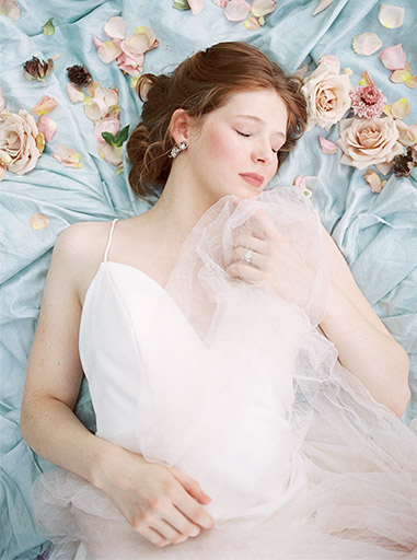 redhead bride laying on blue silk with flowers scattered nearby