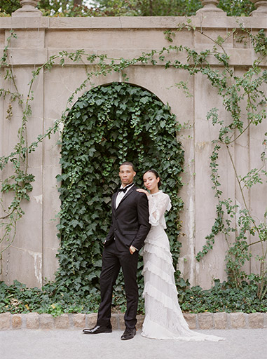 bride and groom posing in front of wall with vines