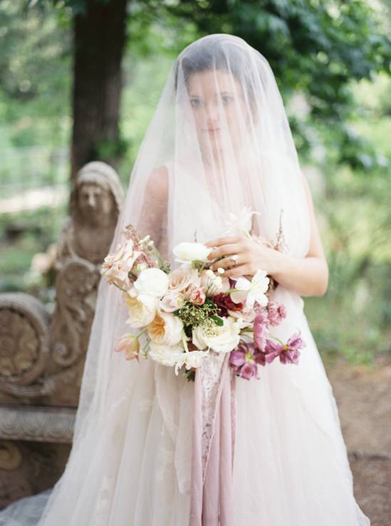 bride draped in white wedding veil holding bouquet