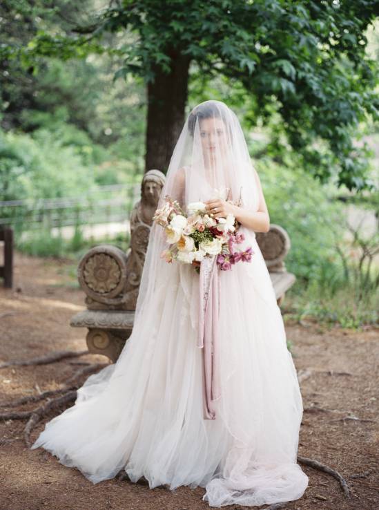 bride draped in wedding veil in front of a lake