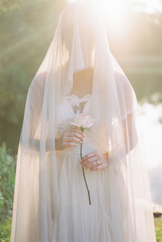 veiled bride holding a single rose in front of a lake