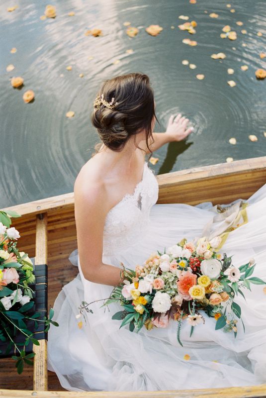 bride holding a bouquet touching the water from a conoe