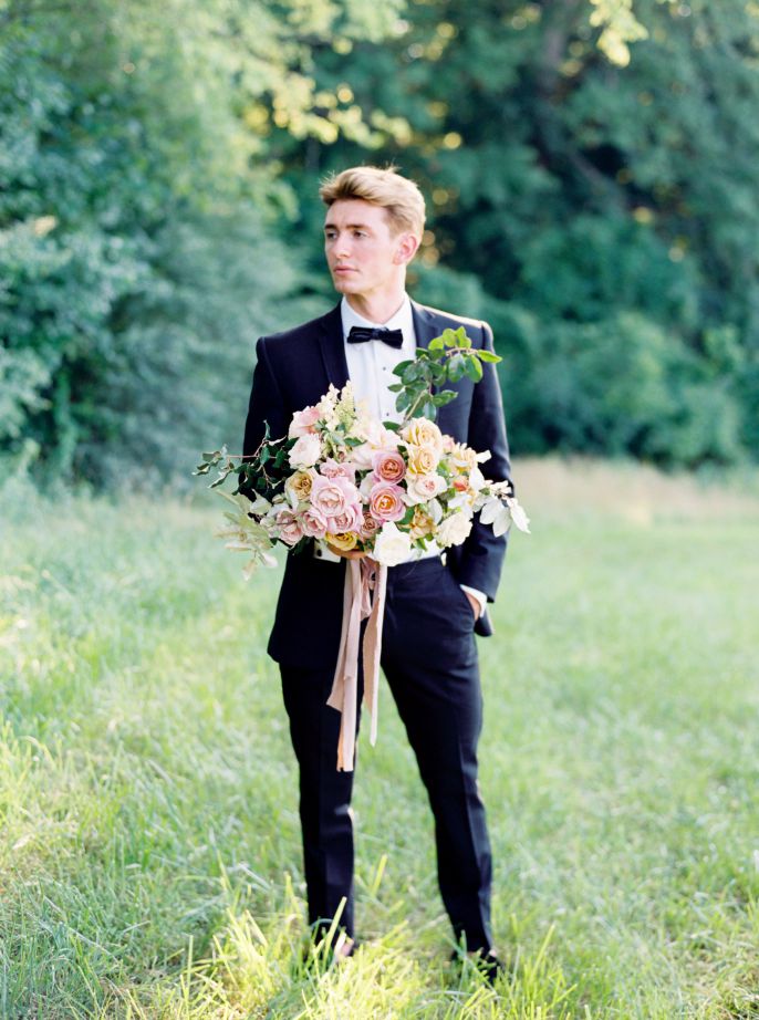 groom in navy suit posing with bridal bouqet