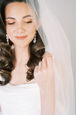 Smiling bride with soft and timeless makeup, her hair down, holding her wedding dress veil.