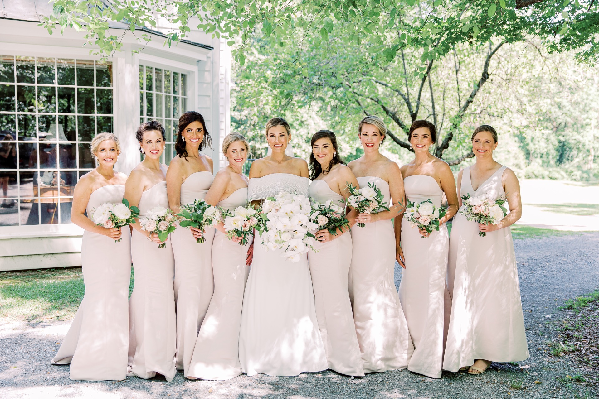 Bride in white and bridesmaids in off-white dresses posing for a portrait in front of the wedding venue