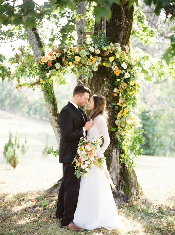 bride and groom embrace in front of tree