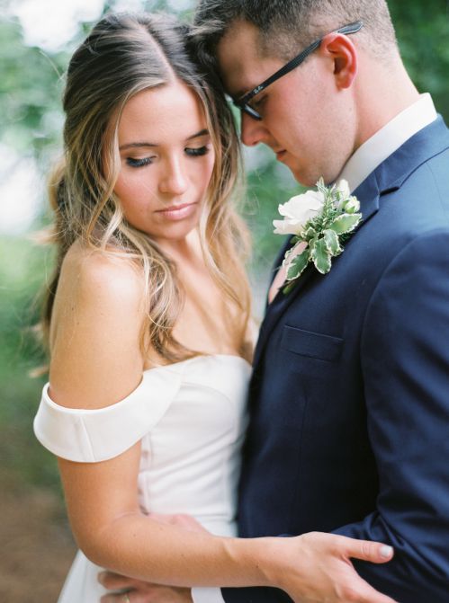 Groom in a navy suit and bride in a white wedding dress embracing before their wedding.