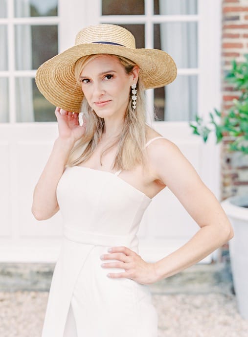 Woman standing in front of white doors with a large hat and white dress