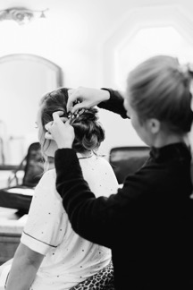 Hair and makeup artist creating an up-do for a bride on her wedding day.