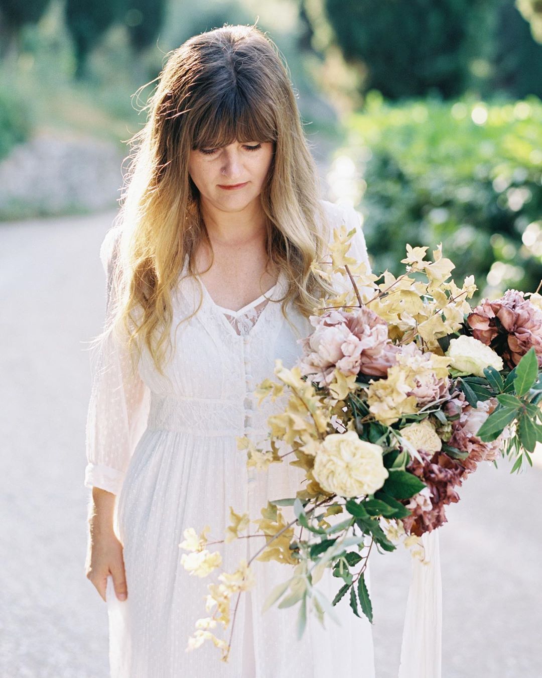 Beautiful bride in a wedding dress, with bangs, holding a large bouquet of flowers walking towards the camera.